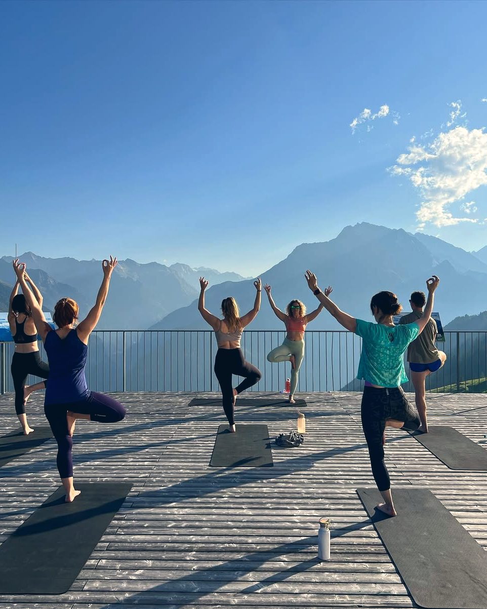 Guests in tree pose on the lodge's open-air deck, the Zillertal peaks beyond.