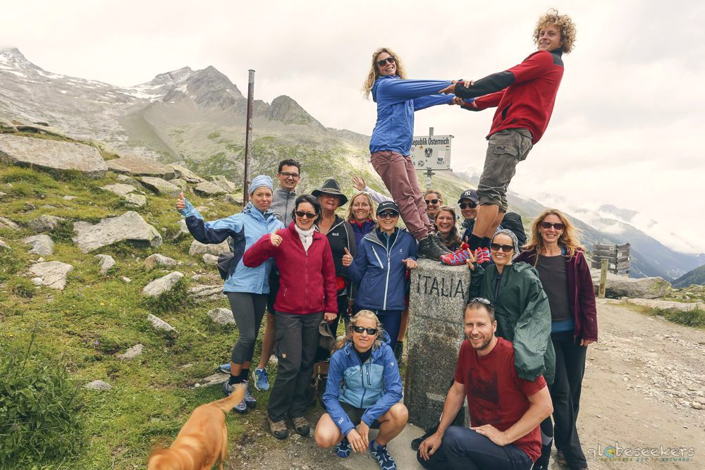 A small group hiking a high alpine trail, glacier-blue peaks all around.