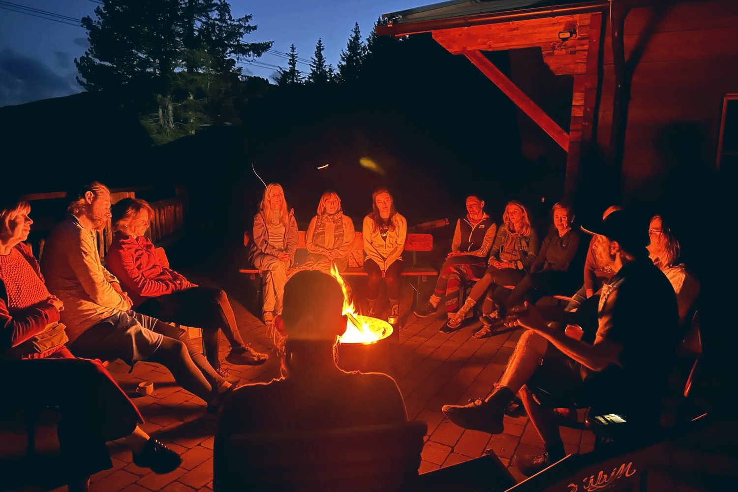 A group gathered around a bonfire by the sea at night.