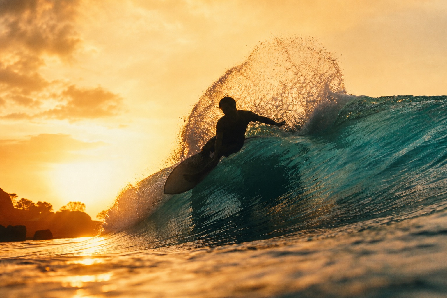 A surfer carves a clean turquoise wave at golden hour, spray catching the light.