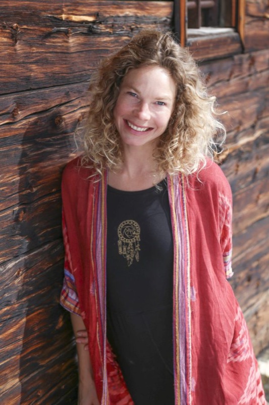 Denise, smiling against a weathered alpine cabin wall.